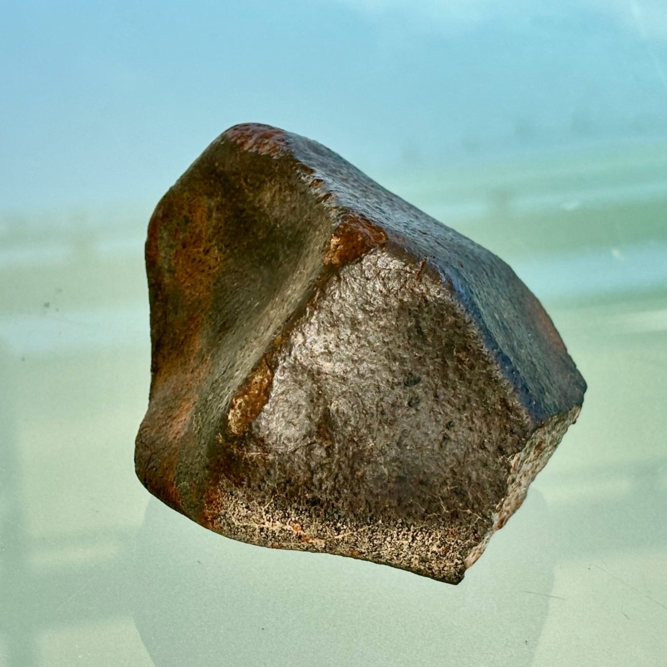 Dunkler, kantiger Meteorit mit silbrig-metallisch glänzender Oberfläche und rostbraunen Verfärbungen vor hellem Hintergrund.
