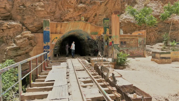 Eingang der historischen Mine Ahouli in Marokko mit buntem Graffiti am Tunneleingang, alten Schienen und inmitten einer felsigen Gebirgsland